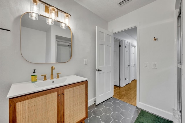 bathroom featuring a textured ceiling, vanity, baseboards, visible vents, and tile patterned floors