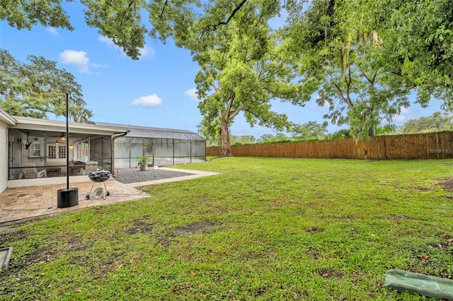 view of yard featuring glass enclosure, a fenced backyard, a patio, and ceiling fan