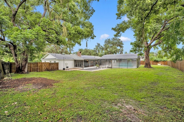 rear view of house featuring a lawn, glass enclosure, a fenced backyard, a chimney, and a patio area