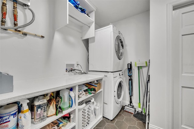 laundry room with laundry area, dark tile patterned floors, and stacked washer and dryer