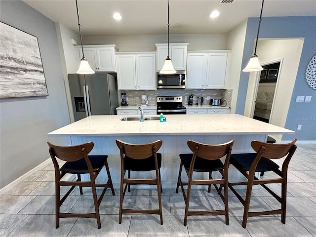 kitchen with stainless steel appliances, white cabinetry, tasteful backsplash, sink, and a kitchen island with sink