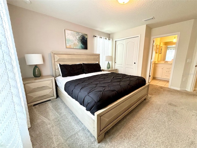 carpeted bedroom featuring a closet, a textured ceiling, and ensuite bath