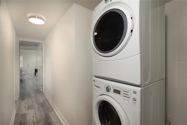 clothes washing area with light hardwood / wood-style floors and stacked washer / dryer