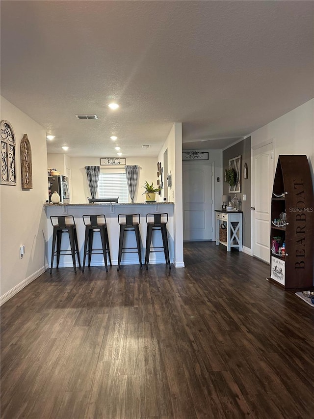 interior space with refrigerator, wood finished floors, visible vents, baseboards, and a kitchen bar