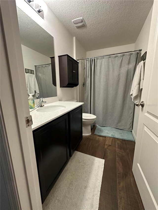 full bathroom featuring toilet, a textured ceiling, vanity, wood finished floors, and a shower with curtain