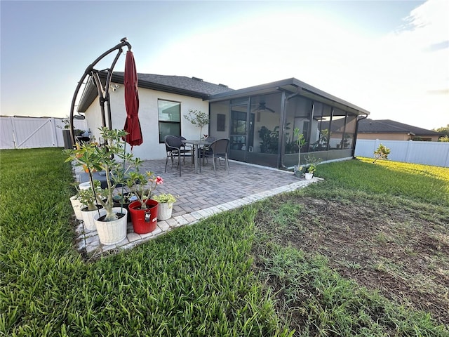 rear view of house with a sunroom, a patio area, a lawn, and stucco siding