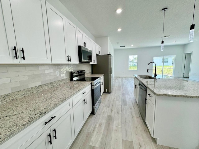 kitchen featuring appliances with stainless steel finishes, decorative backsplash, an island with sink, light hardwood / wood-style floors, and white cabinets