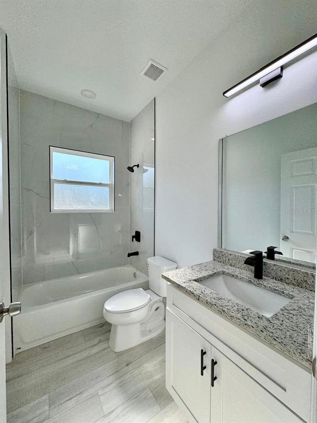 full bathroom with tiled shower / bath, a textured ceiling, vanity, and toilet