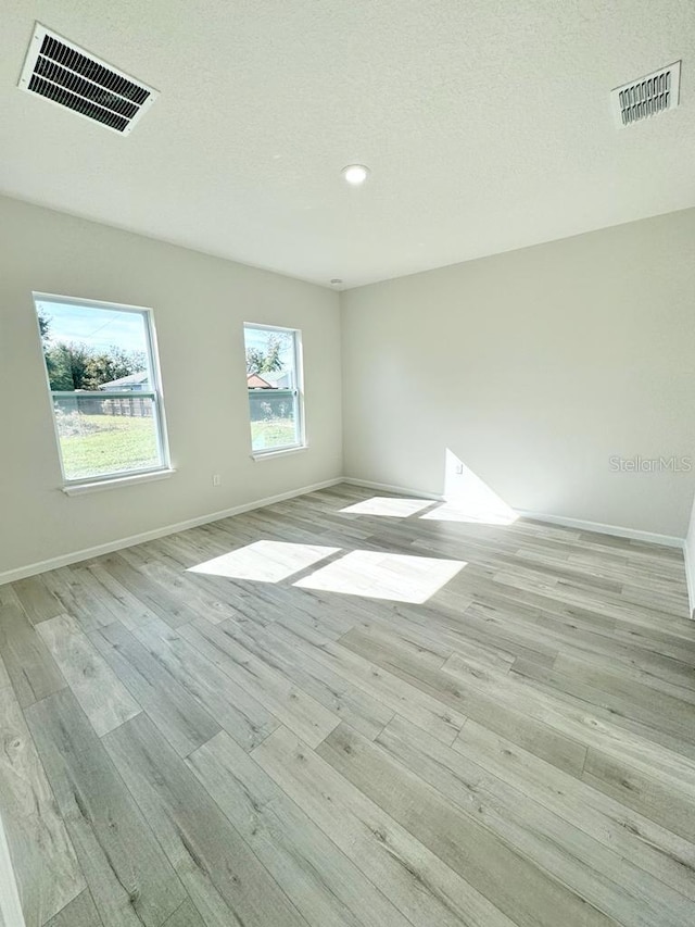 unfurnished room with a textured ceiling and light hardwood / wood-style floors