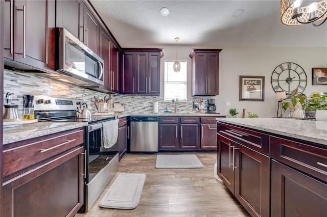 kitchen with light hardwood / wood-style flooring, light stone counters, stainless steel appliances, pendant lighting, and tasteful backsplash