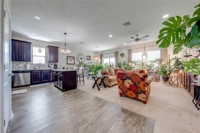 living room featuring a textured ceiling, light colored carpet, sink, and ceiling fan with notable chandelier