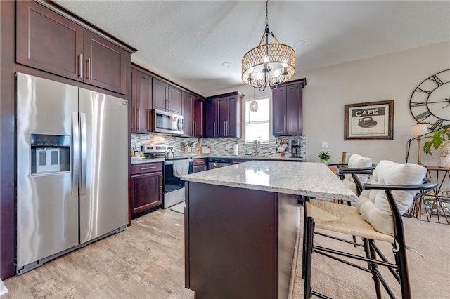 kitchen featuring a notable chandelier, stainless steel appliances, light stone counters, a center island, and a breakfast bar