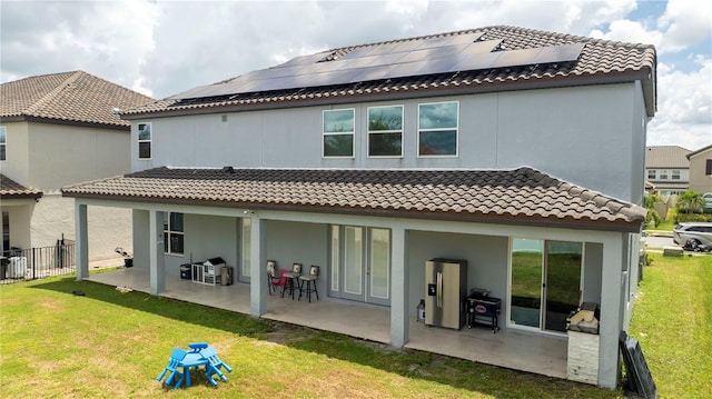 rear view of property with solar panels, a lawn, a patio area, and fence