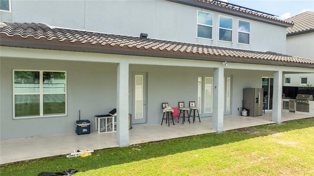 rear view of property featuring a tile roof, a patio area, a yard, and stucco siding