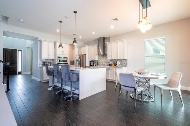 kitchen with wall chimney range hood, a kitchen island, stainless steel appliances, and decorative backsplash