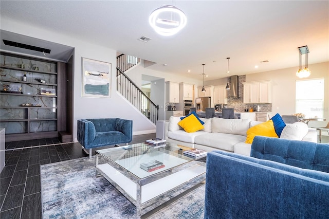 living room with wood tiled floor, visible vents, stairway, and baseboards