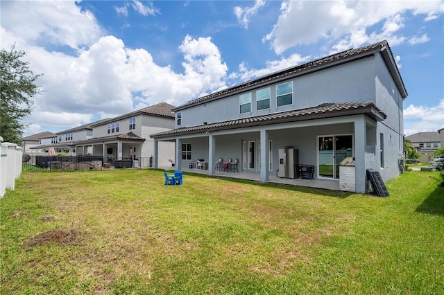 rear view of house featuring a patio, a tile roof, fence, a yard, and stucco siding