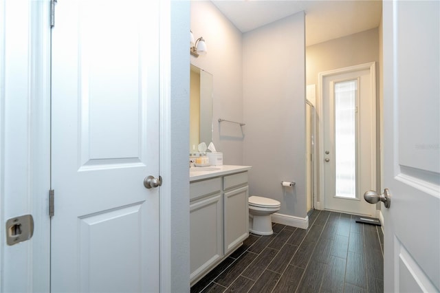 bathroom with toilet, vanity, a shower stall, wood finished floors, and baseboards