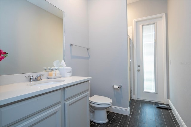 full bath featuring toilet, wood finish floors, vanity, baseboards, and a stall shower