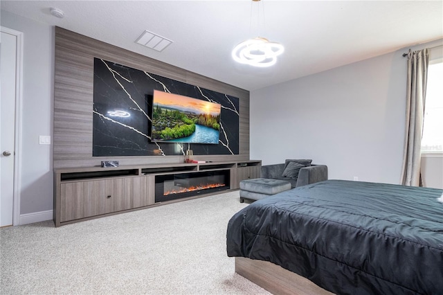 bedroom featuring a glass covered fireplace, light carpet, visible vents, and baseboards