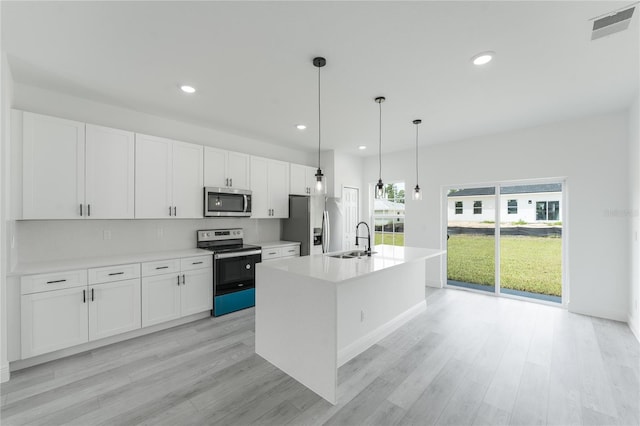 kitchen with white cabinets, appliances with stainless steel finishes, pendant lighting, and a kitchen island with sink