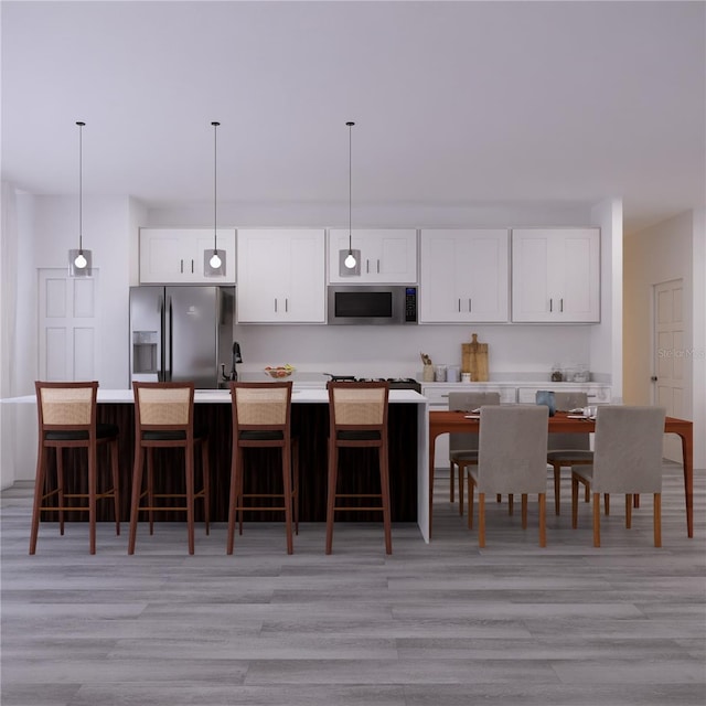 kitchen featuring light wood-type flooring, pendant lighting, stainless steel appliances, an island with sink, and white cabinets