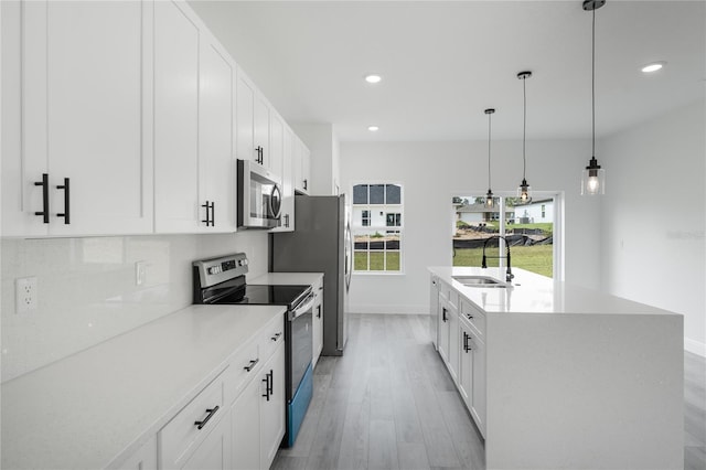 kitchen with stainless steel appliances, sink, hanging light fixtures, a center island with sink, and white cabinets