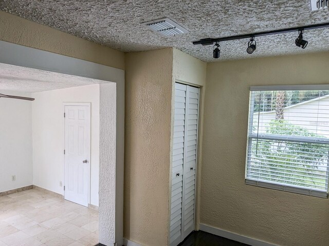 unfurnished bedroom featuring a textured ceiling, track lighting, and tile patterned floors