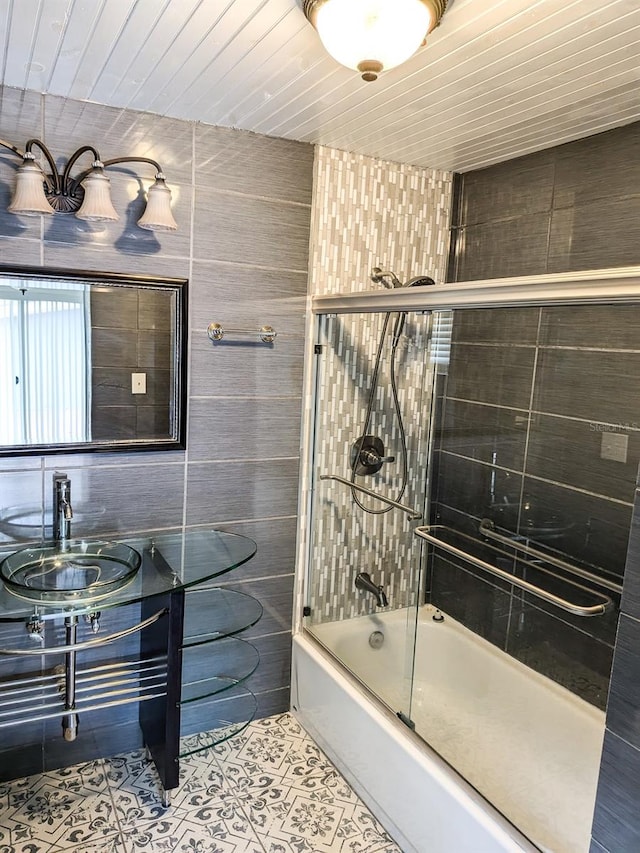 bathroom with sink, tile walls, wooden ceiling, and bath / shower combo with glass door