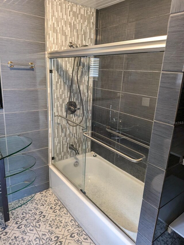 bathroom featuring combined bath / shower with glass door, tile patterned flooring, and tile walls