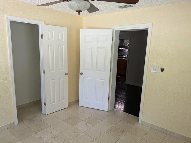 unfurnished bedroom with light tile patterned floors, a closet, a spacious closet, a textured ceiling, and ceiling fan