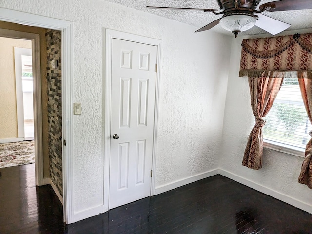 spare room with a textured ceiling, ceiling fan, a healthy amount of sunlight, and dark hardwood / wood-style flooring