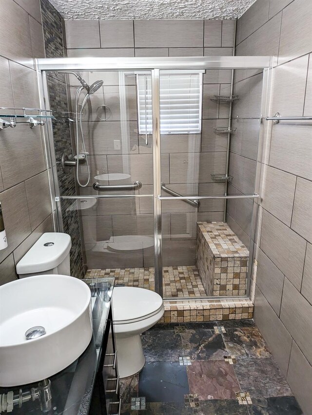 bathroom featuring sink, tile patterned floors, tile walls, toilet, and a shower with door