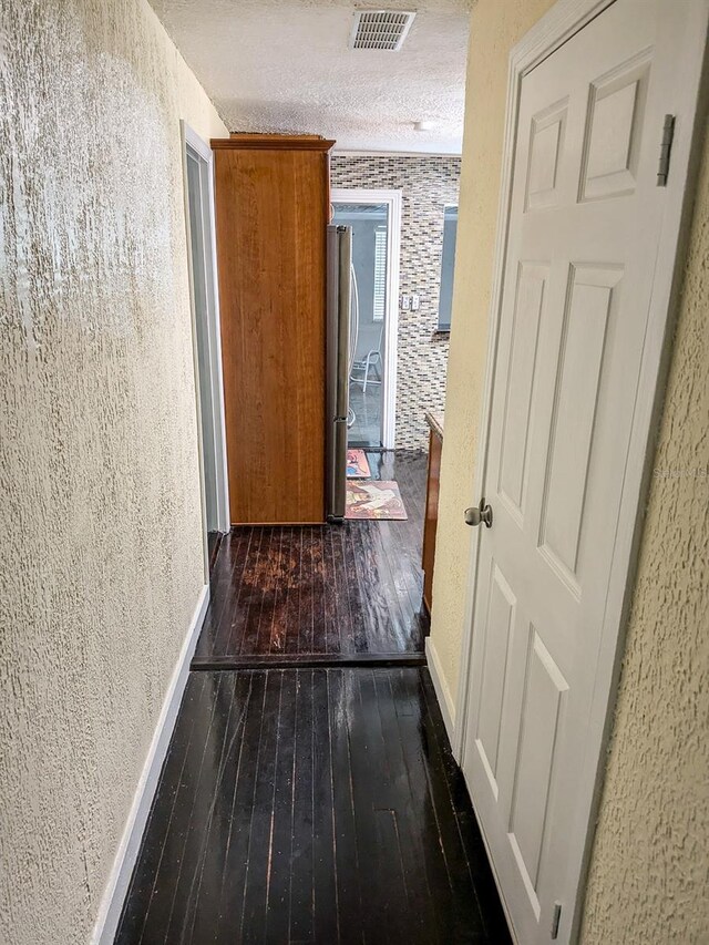 hallway with a textured ceiling and dark hardwood / wood-style floors