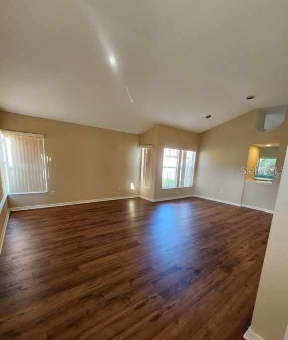 unfurnished room with dark wood-style flooring, vaulted ceiling, and baseboards