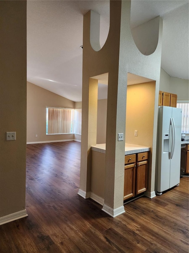 kitchen with dark wood-style floors, lofted ceiling, light countertops, brown cabinetry, and white fridge with ice dispenser