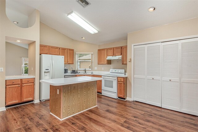 kitchen with vaulted ceiling, a sink, a kitchen island, under cabinet range hood, and white appliances