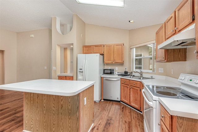 kitchen featuring light wood-type flooring, white appliances, under cabinet range hood, a kitchen island, and a sink