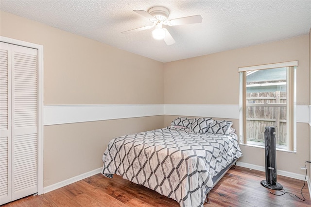bedroom with baseboards, a textured ceiling, a ceiling fan, a closet, and wood finished floors