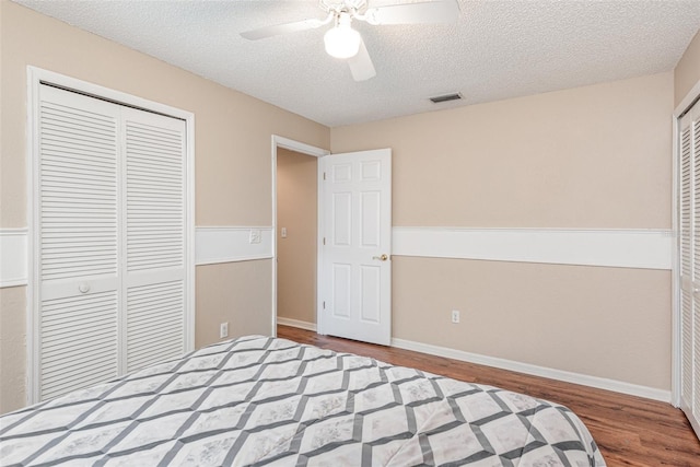 unfurnished bedroom with a closet, a textured ceiling, visible vents, ceiling fan, and wood finished floors