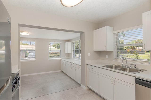 kitchen with appliances with stainless steel finishes, white cabinets, light tile patterned floors, a textured ceiling, and sink