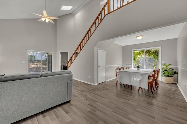 living room featuring ceiling fan, high vaulted ceiling, wood-type flooring, and a skylight