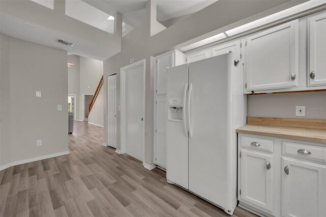 kitchen with white fridge with ice dispenser, light hardwood / wood-style floors, and white cabinets