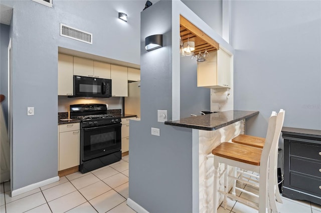 kitchen with a breakfast bar area, black appliances, light tile patterned floors, kitchen peninsula, and cream cabinetry