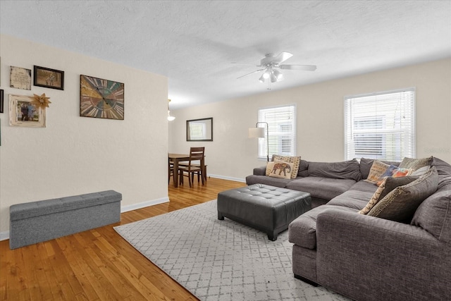 living room with light wood-type flooring, a wealth of natural light, ceiling fan, and a textured ceiling