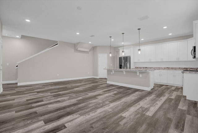 kitchen featuring dark wood-style floors, a kitchen island with sink, stainless steel appliances, white cabinetry, and pendant lighting