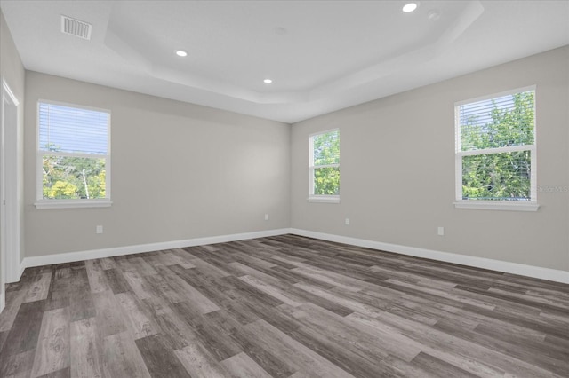 empty room with recessed lighting, a raised ceiling, visible vents, wood finished floors, and baseboards