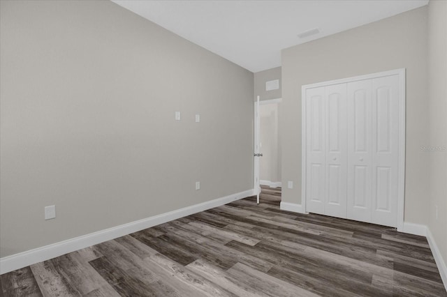 unfurnished bedroom featuring dark wood-style flooring, a closet, visible vents, and baseboards