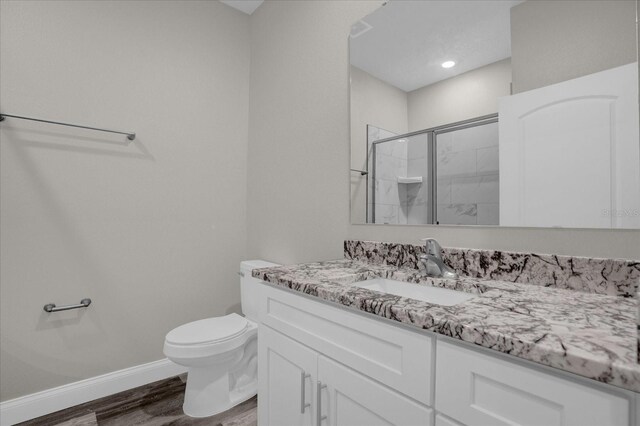 bathroom with a stall shower, baseboards, toilet, wood finished floors, and vanity