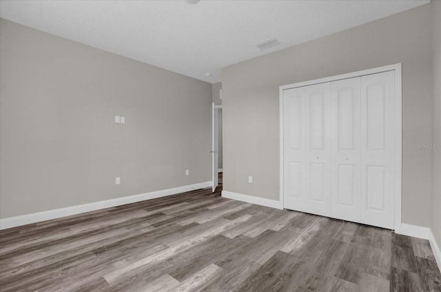 unfurnished bedroom with a closet, visible vents, baseboards, and wood finished floors